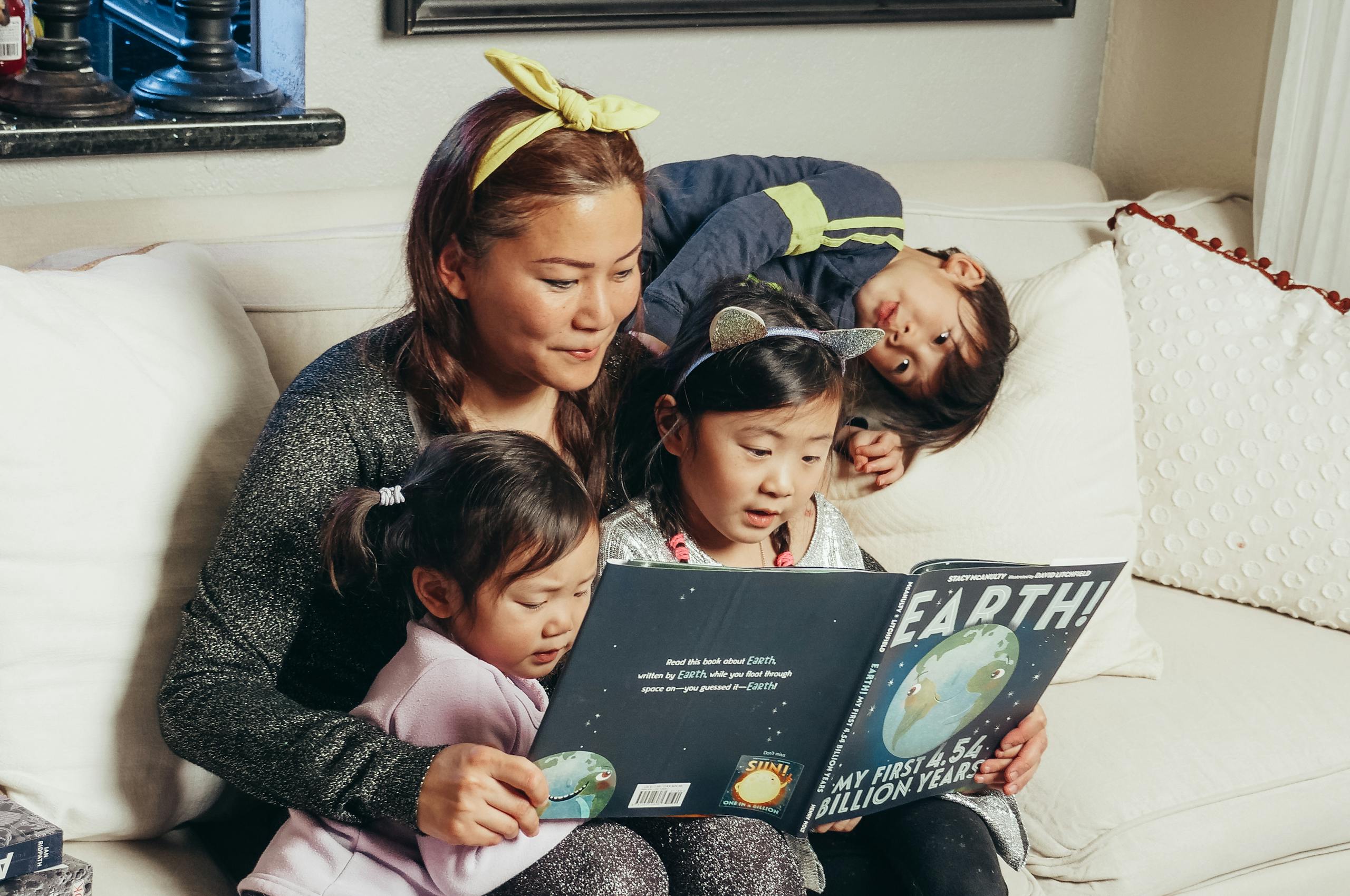 A mother and her children enjoy a book together on a comfortable living room sofa.